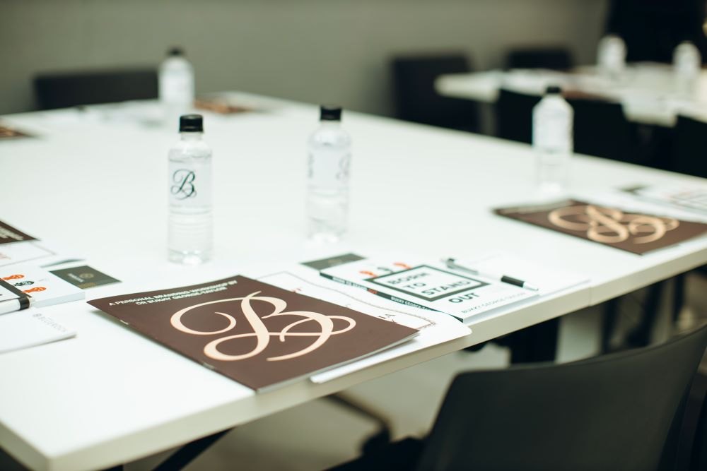 Branded event materials, copies of Born To Stand Out, pens and water bottles arranged on a conference table.