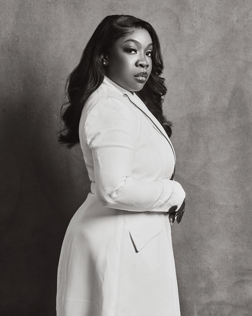 Black-and-white portrait of Dr. Bukky George-Taylor looking over her shoulder in a white blazer.