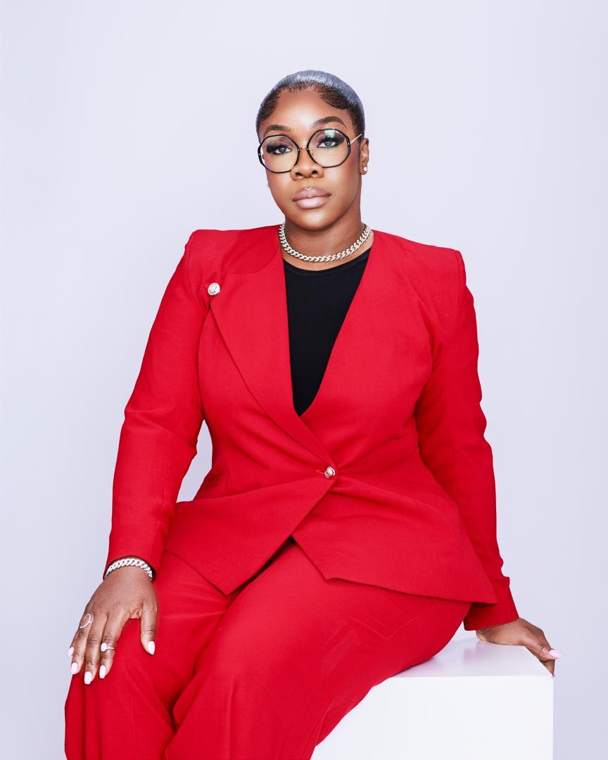 Dr. Bukky George-Taylor seated in a red suit and round glasses.