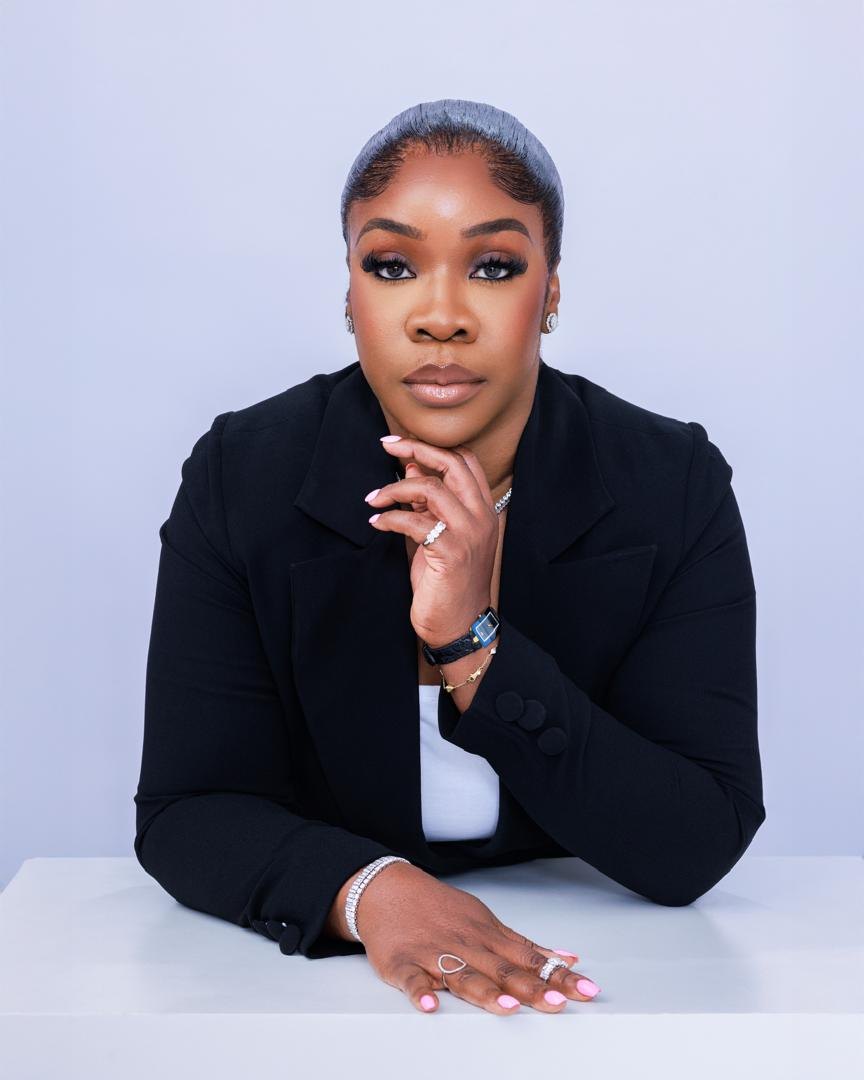 Dr. Bukky George-Taylor in a black blazer, resting her chin on one hand at a white table.